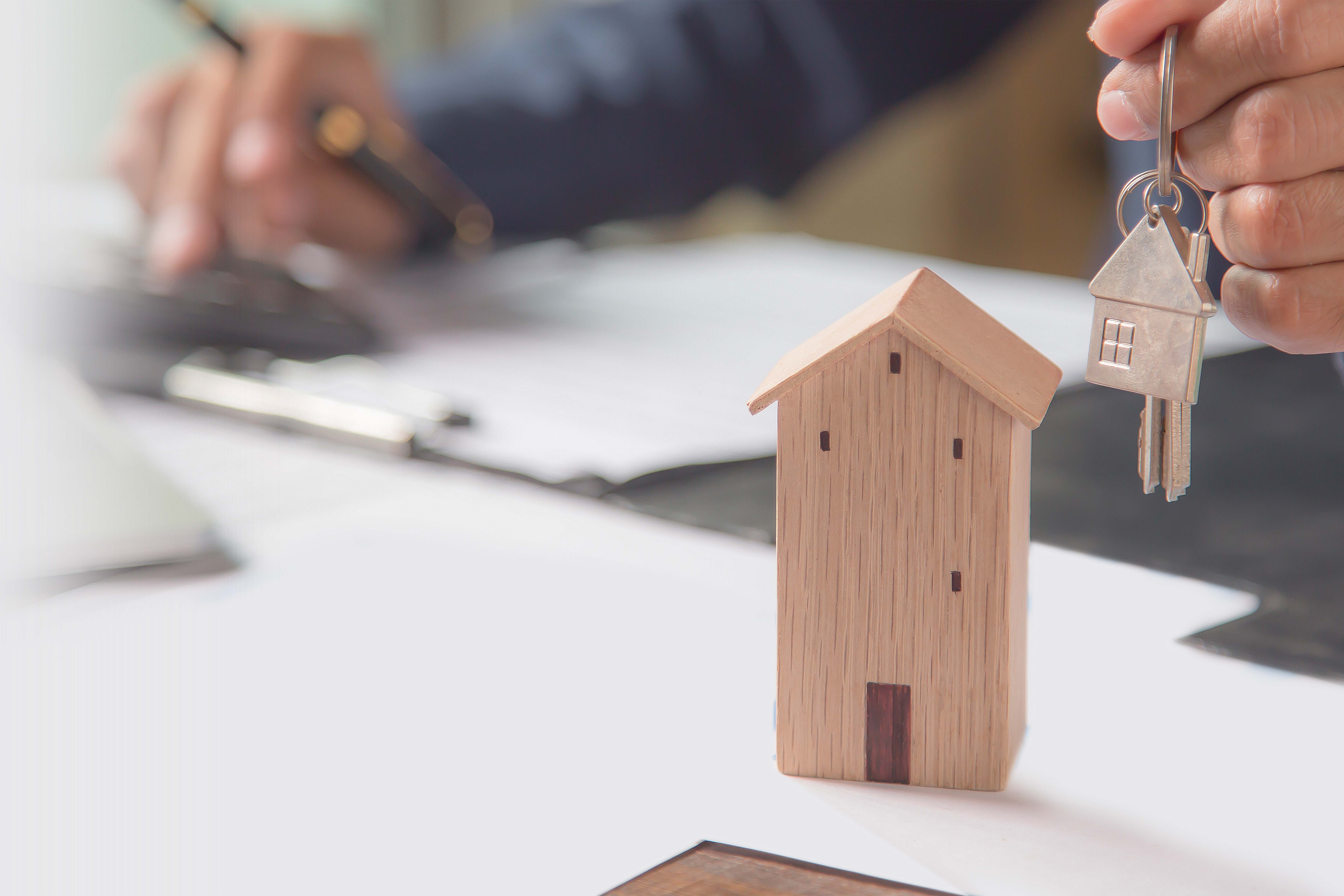  small wooden house ornament with hands holding house keys 